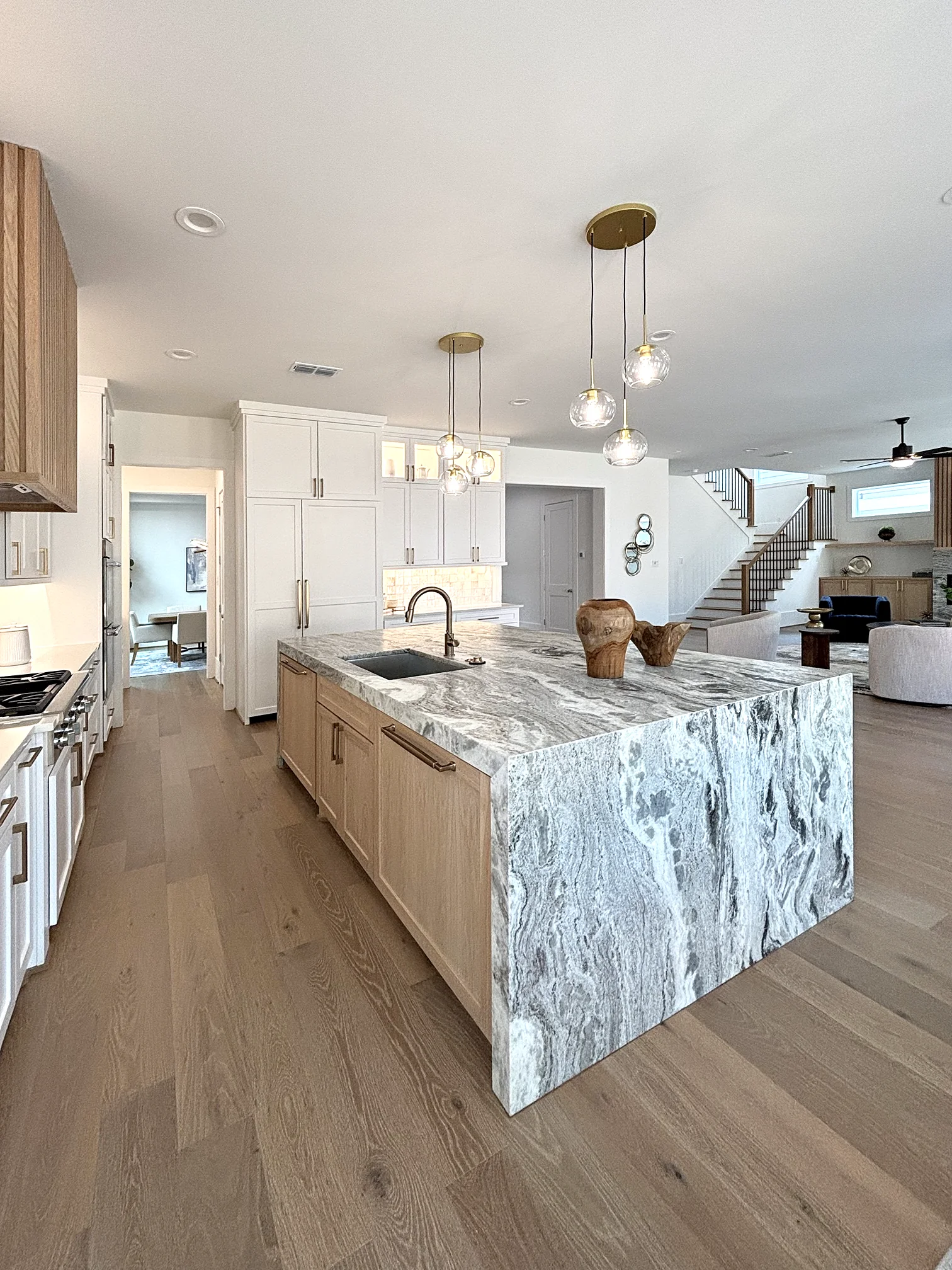 Kitchen island with linear pendant lighting beside an open staircase